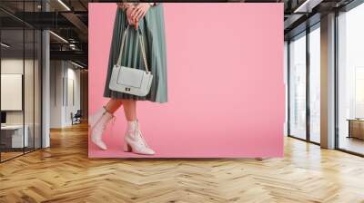 Women`s fashion concept: model wearing trendy white lace up ankle boots, pleated skirt, holding stylish small green mint color faux leather bag, posing on pink background. Copy, empty space for text Wall mural